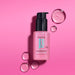 Pink bottle of Matrix InstaCure hair oil with droplets on a pink background